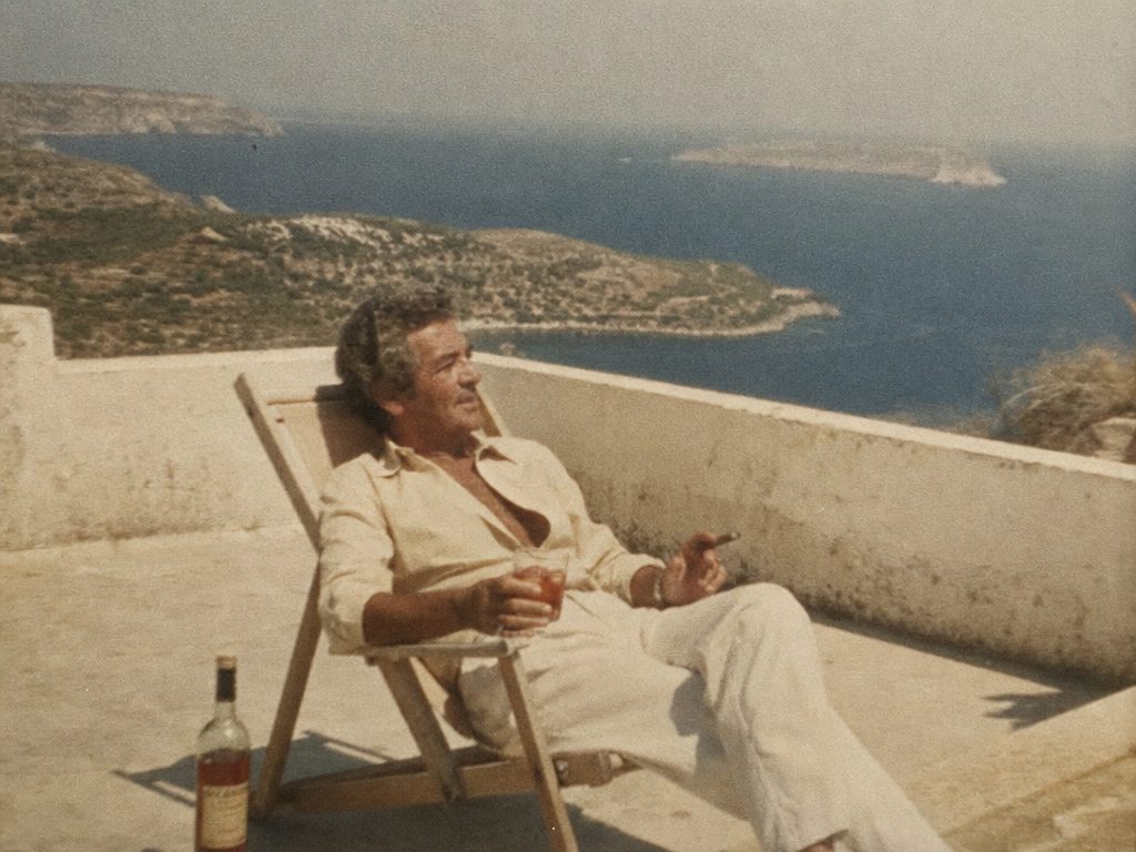 Man in a deck chair on a terrace above the sea, with a cigar and a drink. Generated in Image GPT.