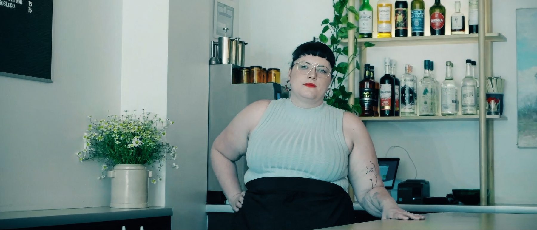 Restaurant owner standing behind her empty bar, looking into the camera